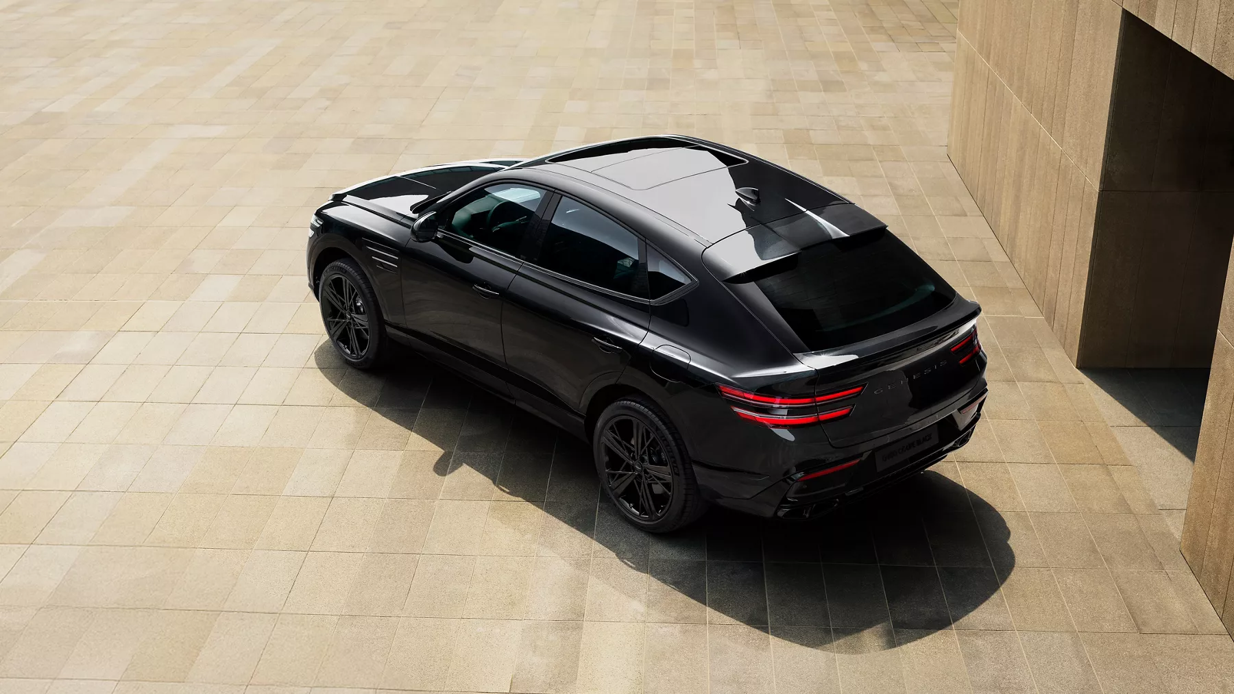 Rear overhead 3/4 view of 2026 Genesis GV80 Coupe Prestige Black parked on beige tiles