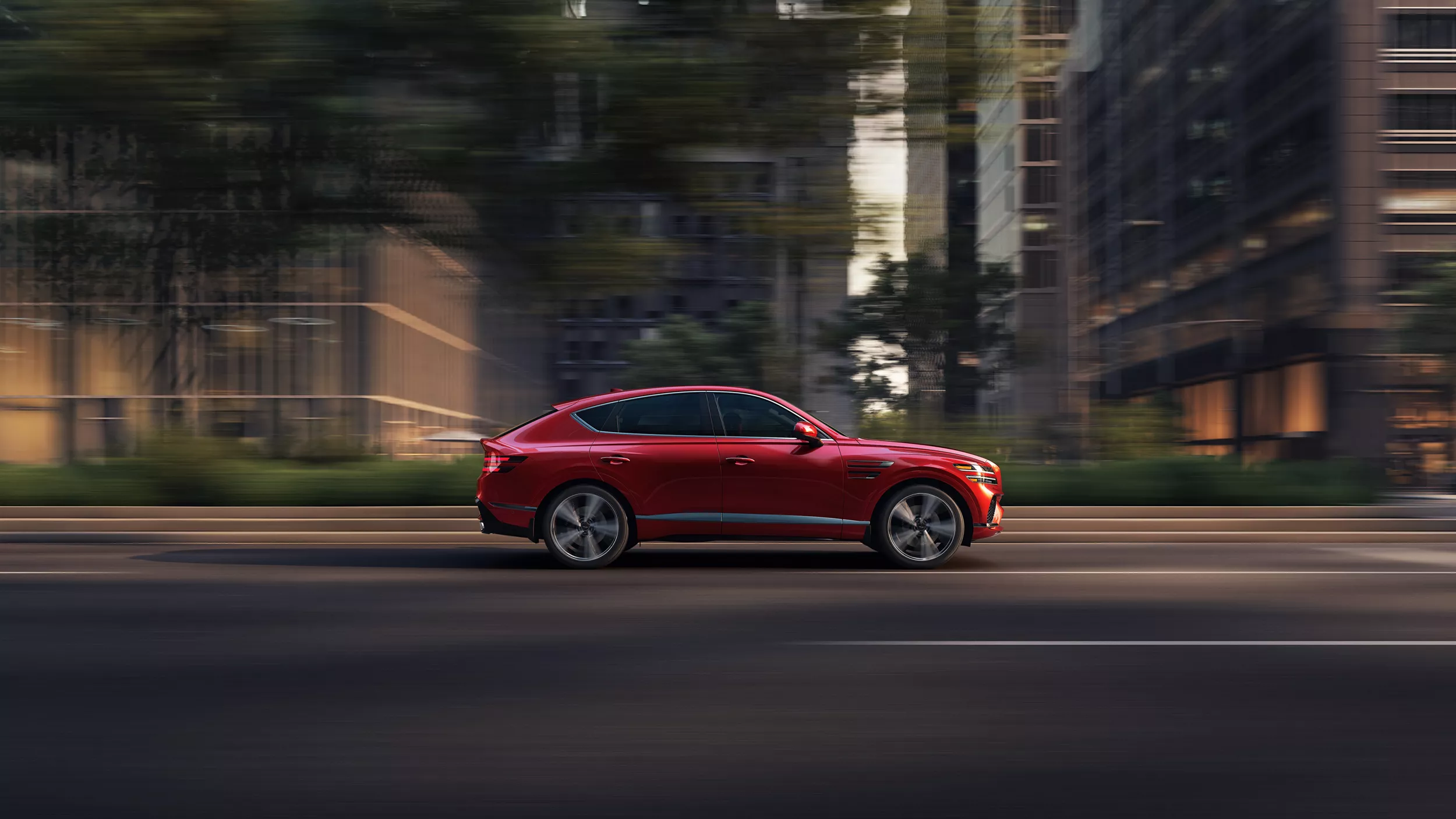 Passenger side profile view of Genesis GV80 Coupe in Mauna Red driving on a city street