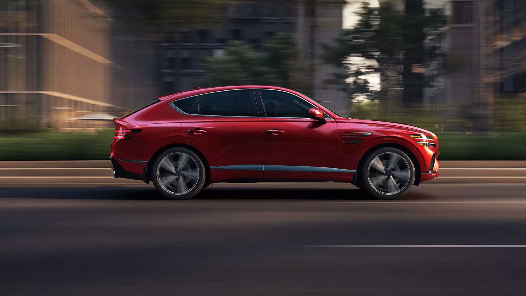 Passenger side profile view of 2026 Genesis GV80 Coupe in Mauna Red driving on an city street