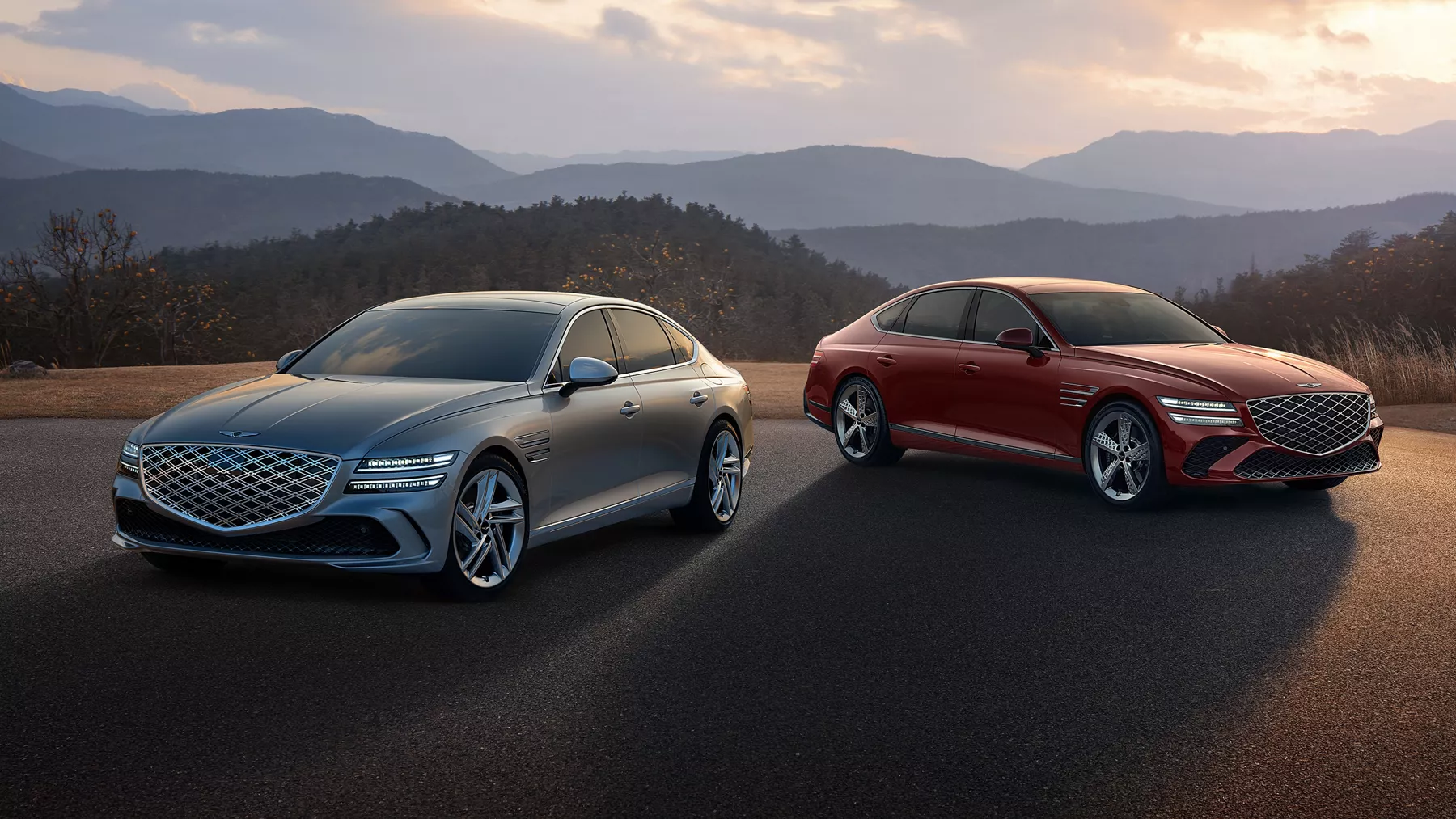 Two 2026 Genesis G80 sedans parked in V-shaped configuration at sunset with mountains in background