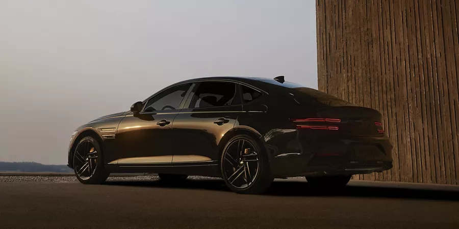 7/8 rear driver side view of 2026 Genesis G80 Prestige Black parked in front of modern building