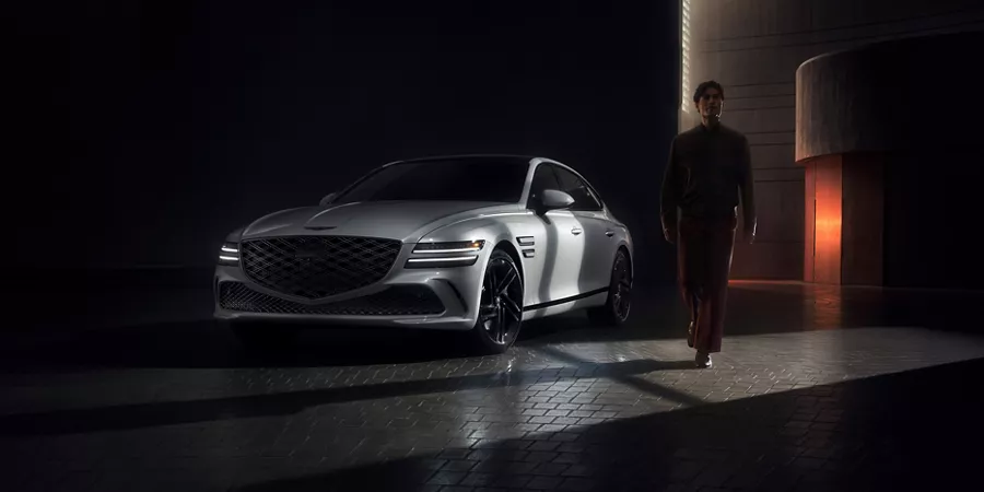 3/4 front driver side view of Genesis G80 Prestige Black in dark room, silhouette of man walking past