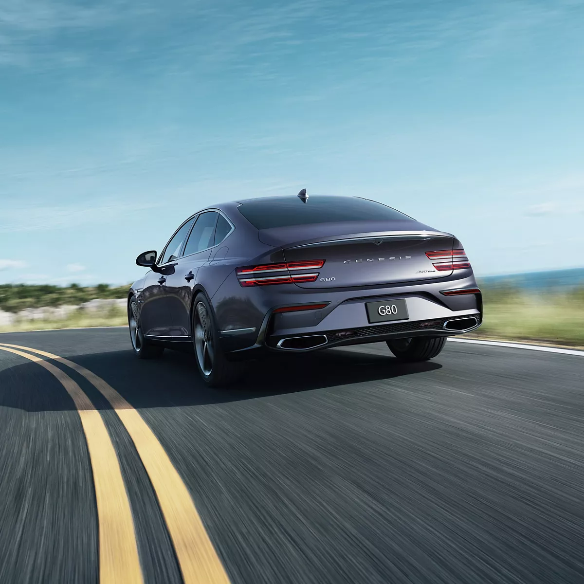 Motioned blurred 3/4 rear driver side view of Genesis G80 driving along coastal highway
