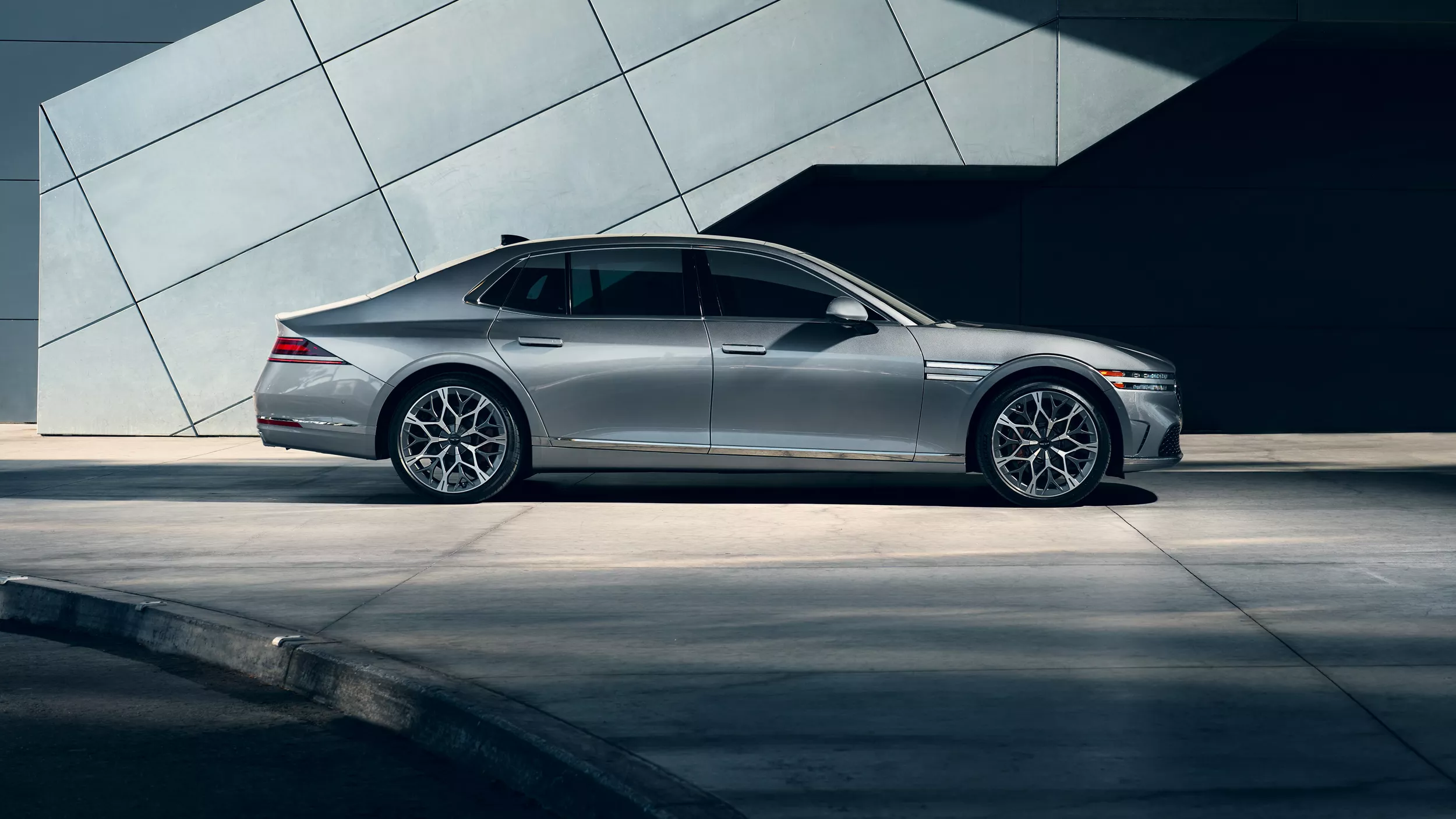 Exterior passenger side profile view of 2026 Genesis G90 in Savile Silver next modern metal building