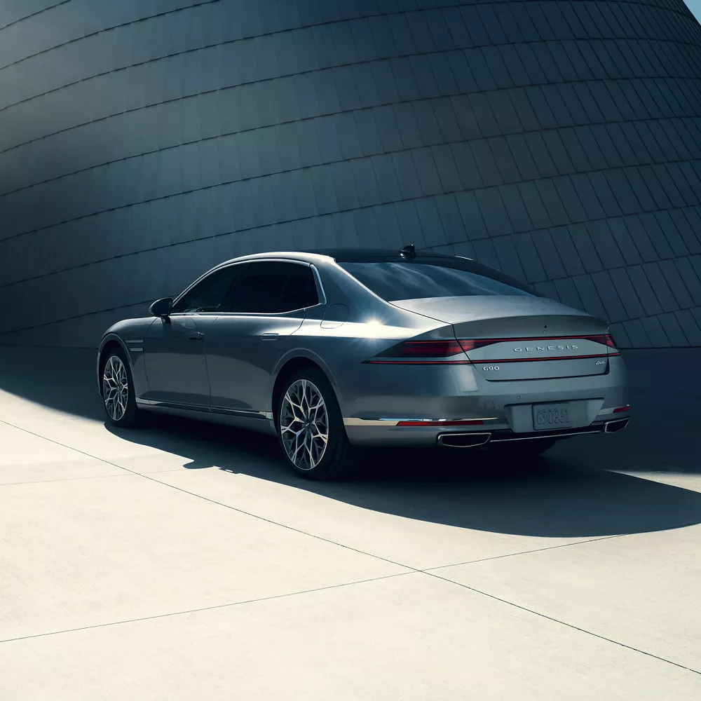 7/8 rear driver side view of 2026 Genesis G90 in Savile Silver in front of modern metal building