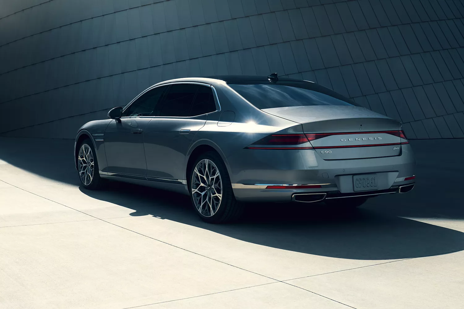 7/8 rear driver side view of 2026 Genesis G90 in Savile Silver in front of modern metal building