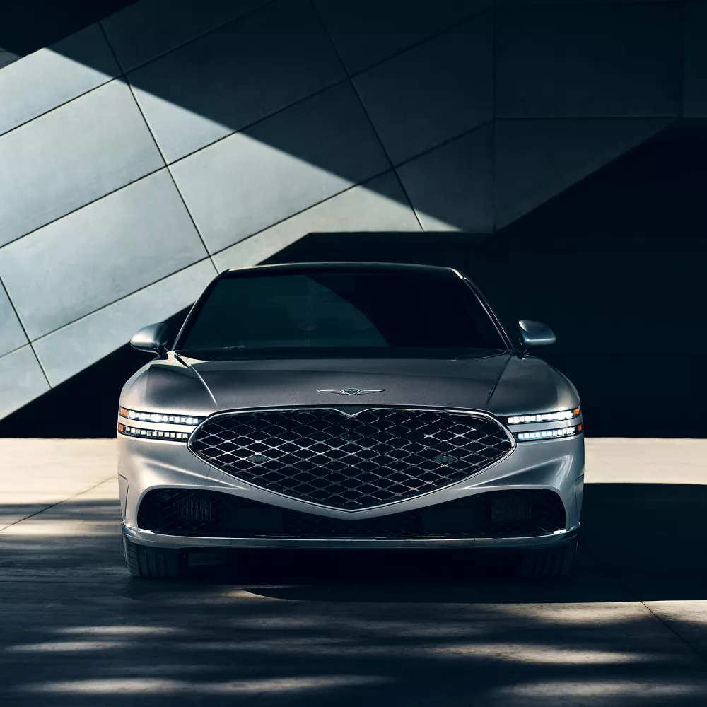 Head on front angle of 2026 Genesis G90 in Savile Silver parked in front modern metal building