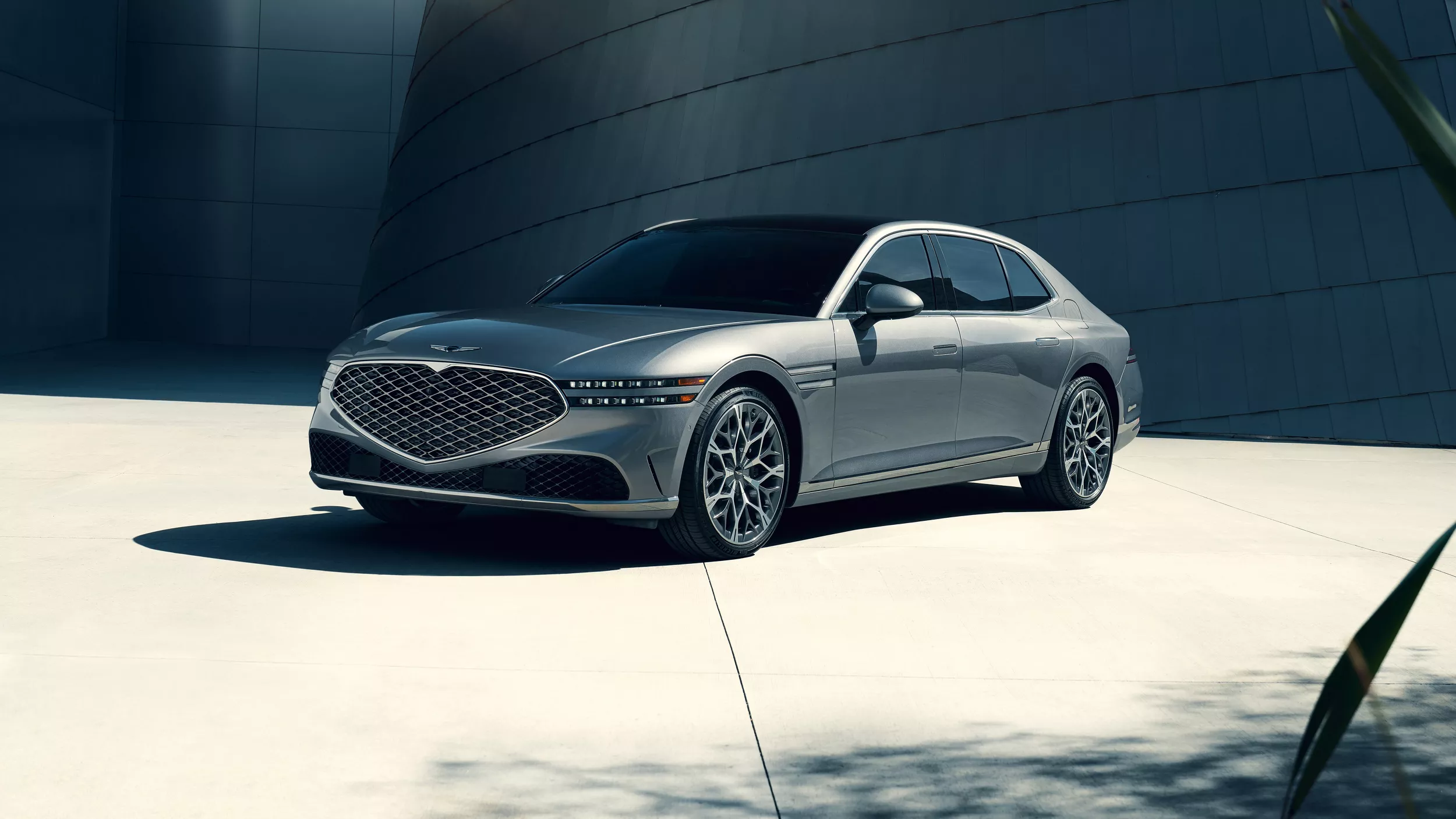 3/4 front driver's side view of 2026 Genesis G90 in Savile Silver parked in front of modern building