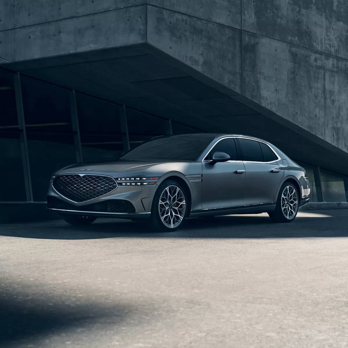 3/4 front driver side view of Genesis G90 in Savile Silver parked under modern concrete structure