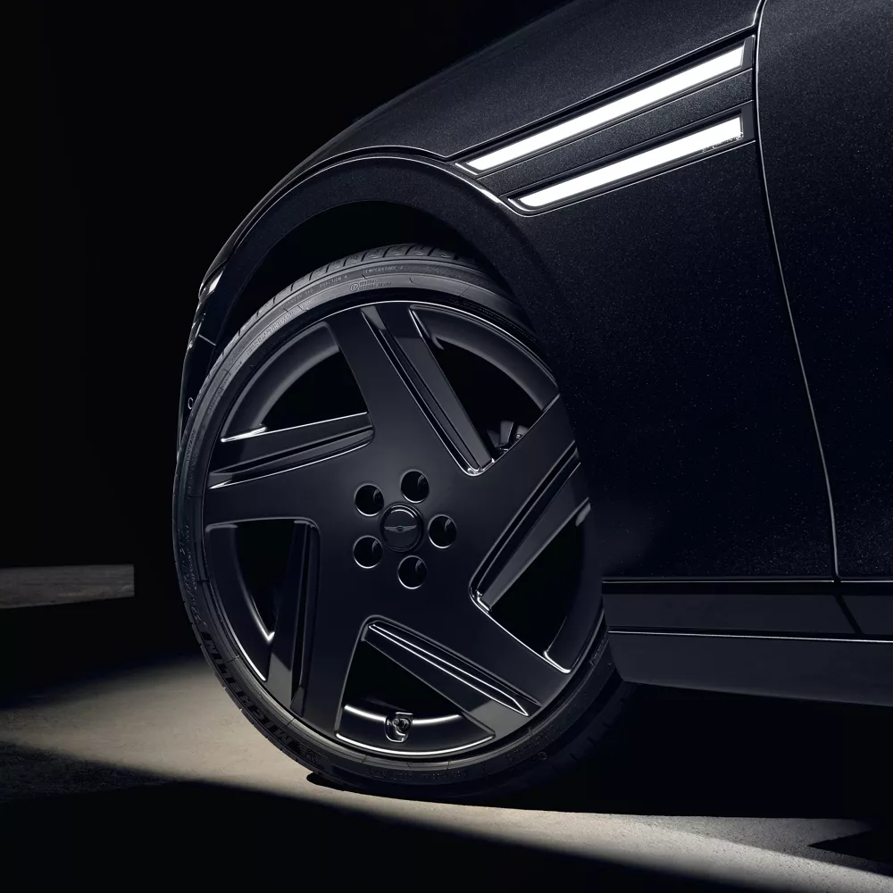 Wheel close up of 2026 Genesis G90 in Prestige Black parked in a dimly lit parking garage