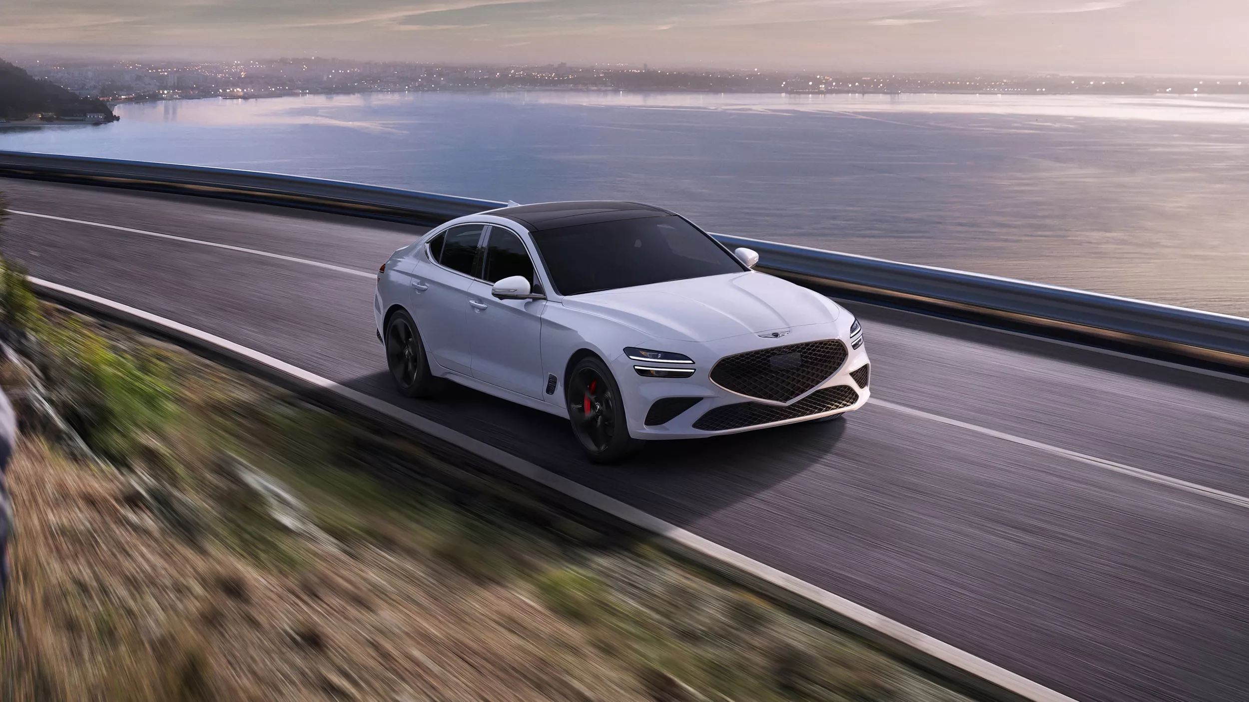 3/4 front passenger side view of 2027 Genesis G70 in Uyuni White driving along a coastal highway