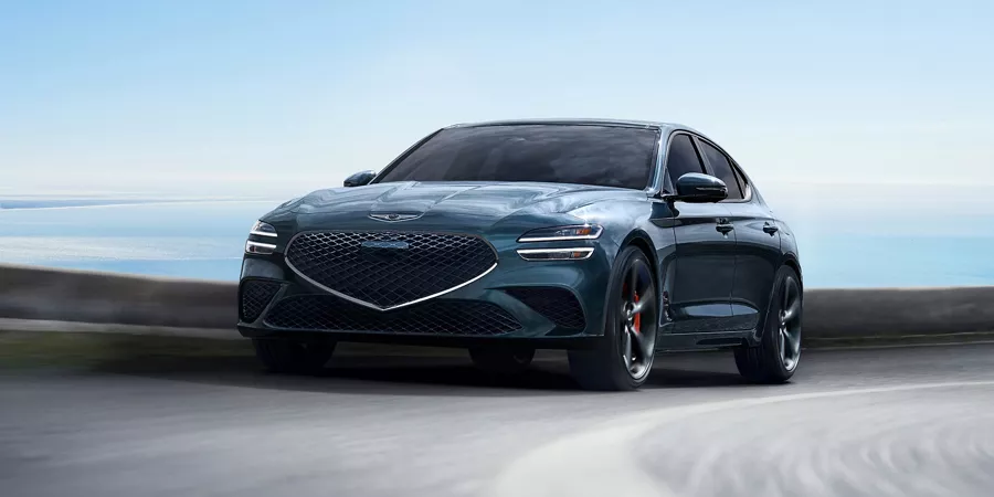 3/4 front driver side view of 2027 Genesis G70 in Tasman Blue in motion driving on a track