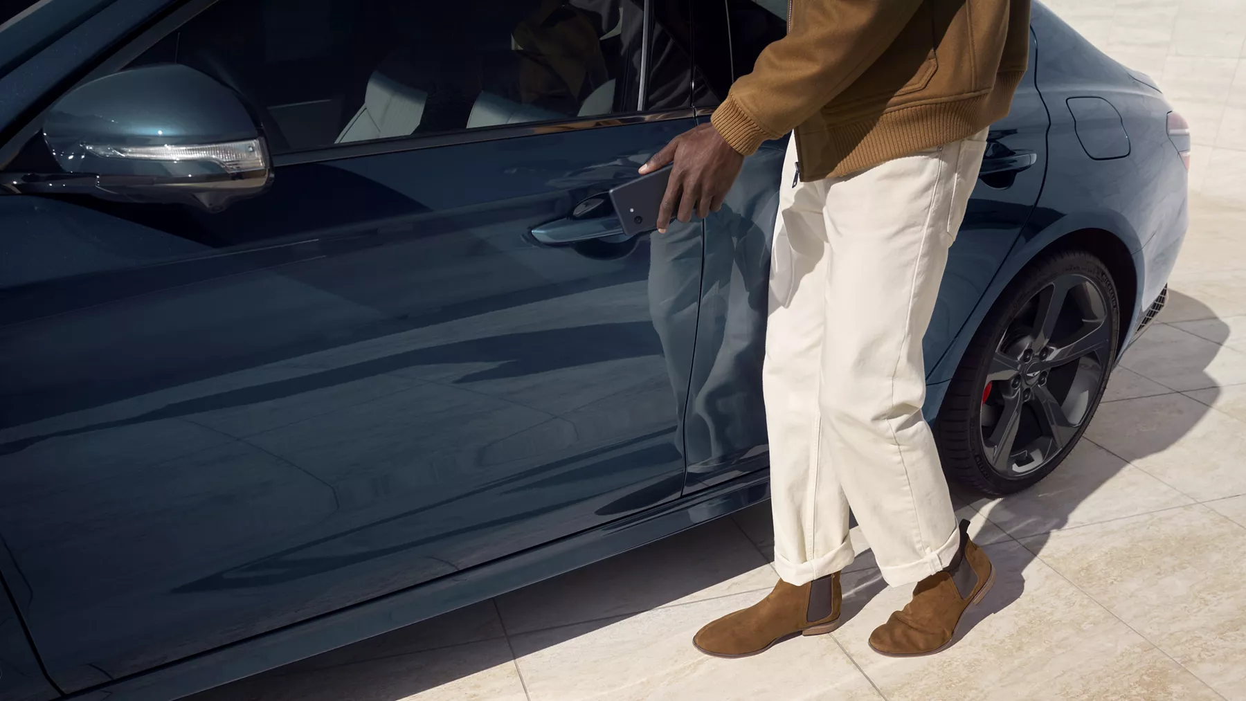 Driver side close up of man holding cell phone up to door handle on 2027 Genesis G70 in Tasman Blue