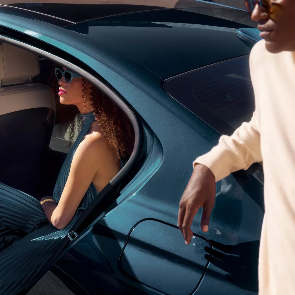 3/4 rear driver side close up of 2027 Genesis G70 in Tasman Blue, woman sitting in back seat