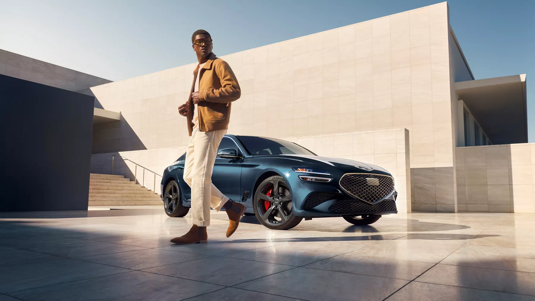 3/4 front passenger side view of 2027 Genesis G70 in Tasman Blue parked at modern home, man nearby