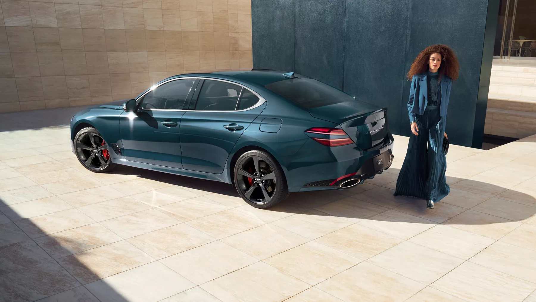 Driver side profile view of 2027 Genesis G70 in Tasman Blue, woman in blue dress standing behind