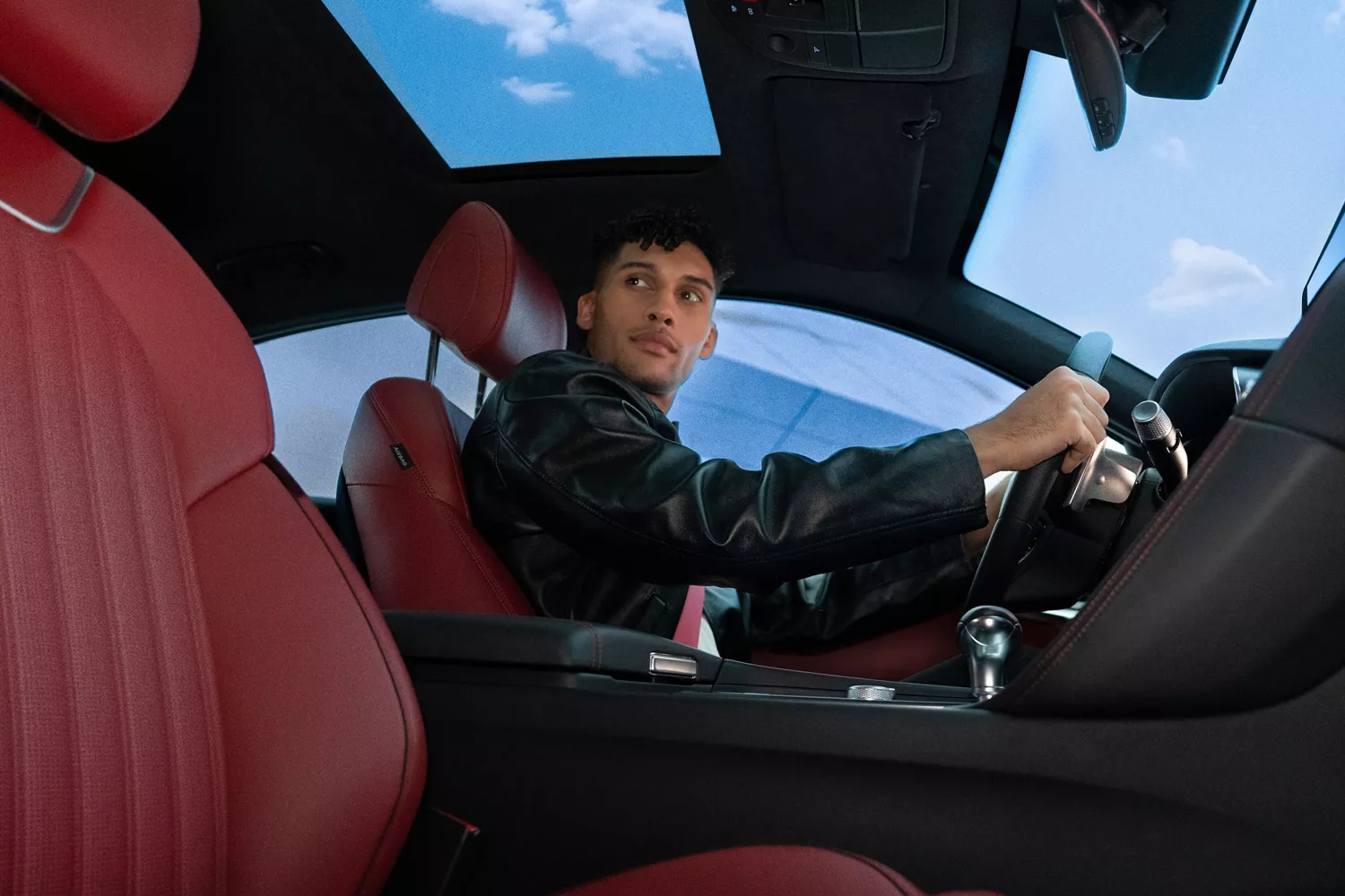 Interior view from passenger seat of man driving 2027 Genesis G70 with Sevilla Red leather seating