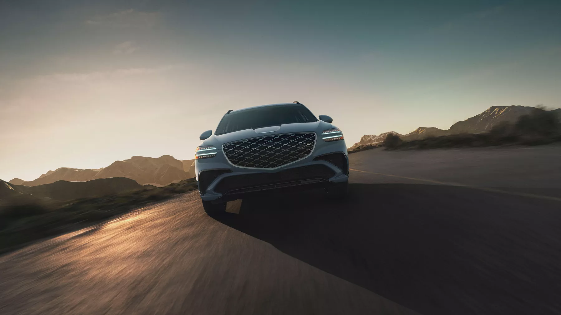 Low front angle view of Genesis GV70 in Bering Blue driving on desert road at dusk