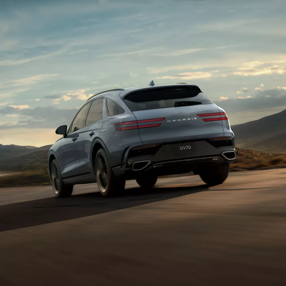 3/4 rear driver side view of Genesis GV70 in Bering Blue road at dusk, with mountains in background
