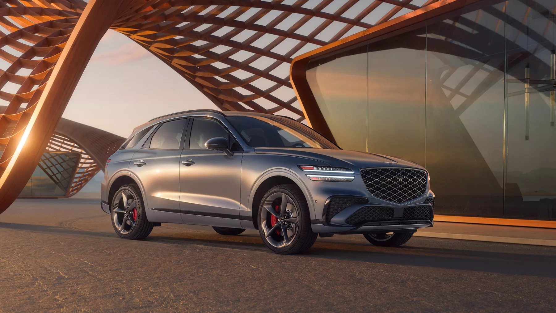 3/4 front passenger side view of Genesis GV70 in Ceres Blue Matte beneath modern structure in desert