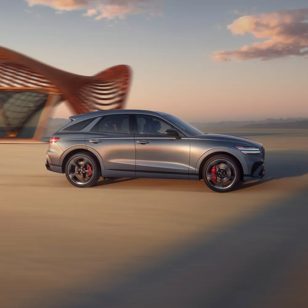 Passenger profile view of Genesis GV70 in Ceres Blue parked in desert beside modern copper structure