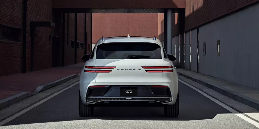 Rear shot of Genesis GV70 in Uyuni White, parked parked between two brick buildings with crosswalk