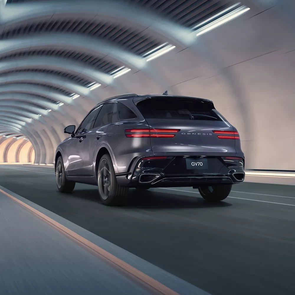 3/4 rear driver view of Genesis GV70 driving inside a futuristic tunnel setting