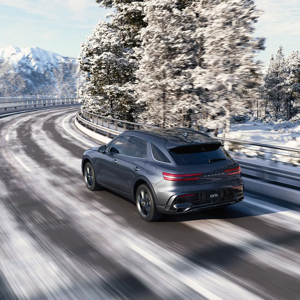 3/4 rear driver side view of gray Genesis GV70 driving on snowy mountain road