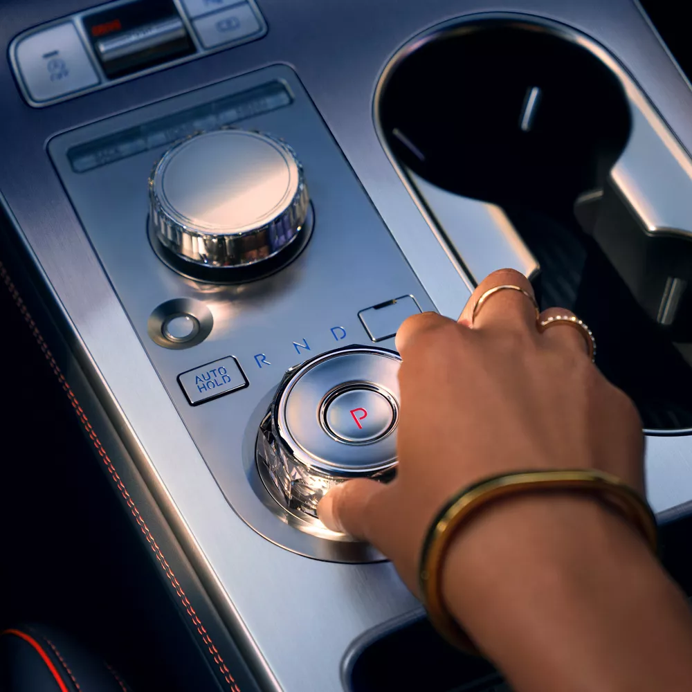 Interior close-up of Genesis GV70 center console, hand using shift by wire gear shifter