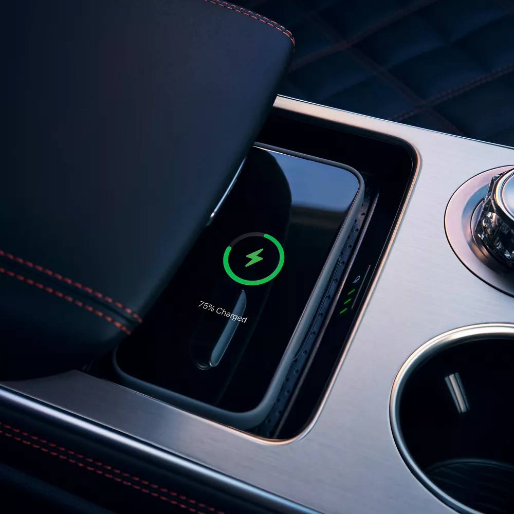 Interior close-up of cell phone charging on wireless charging mat beneath armrest on center console