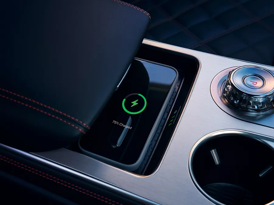 Interior close-up of cell phone charging on wireless charging mat beneath armrest on center console