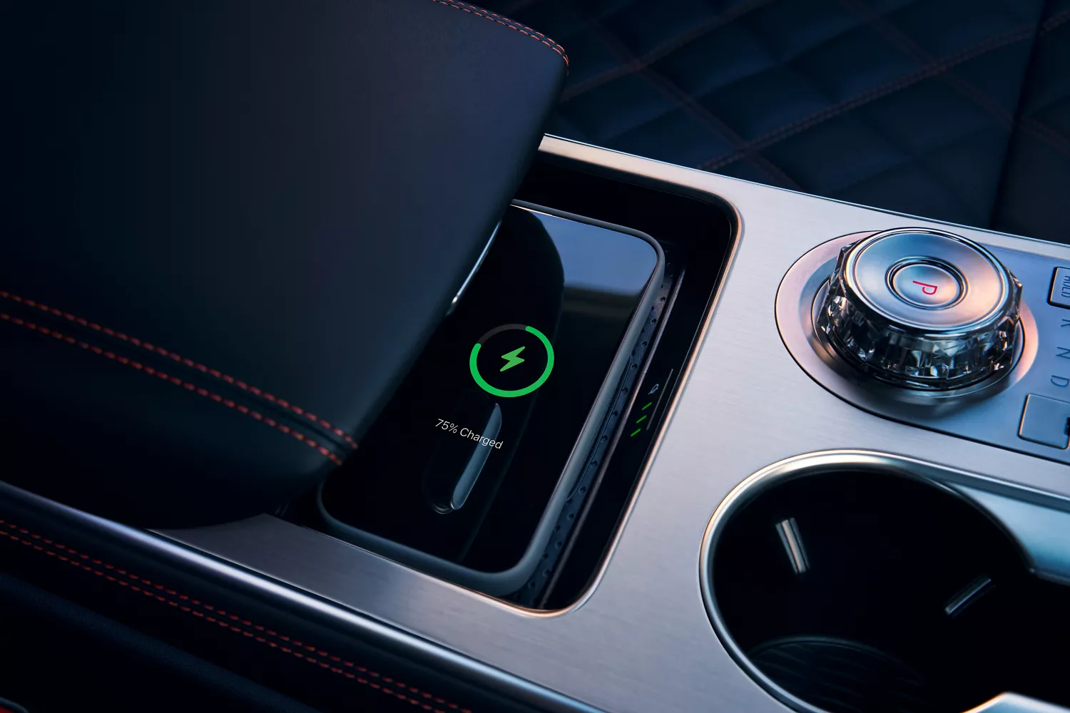 Interior close-up of cell phone charging on wireless charging mat beneath armrest on center console