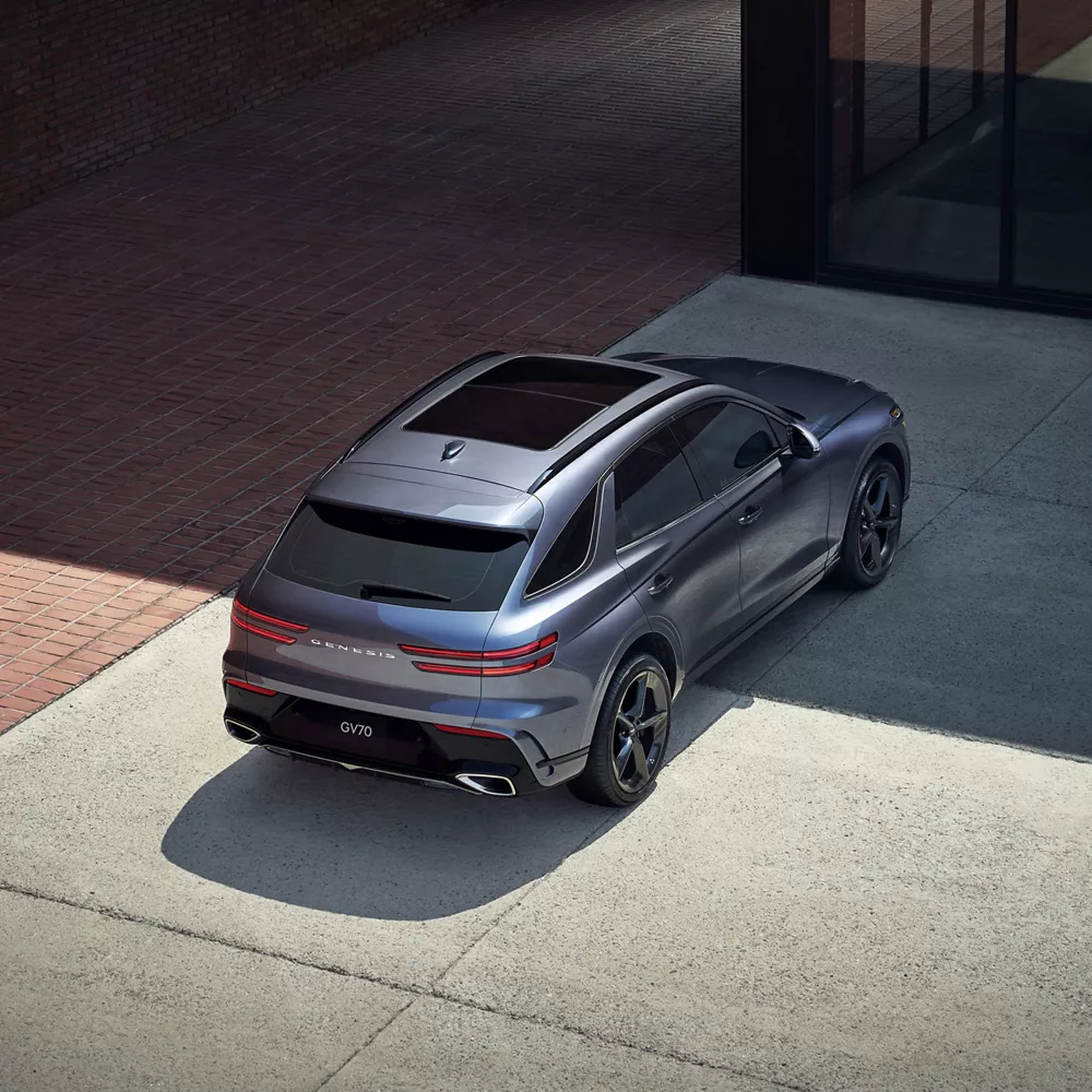 3/4 rear aerial passenger side view of Genesis GV70 in gray parked in front of modern building