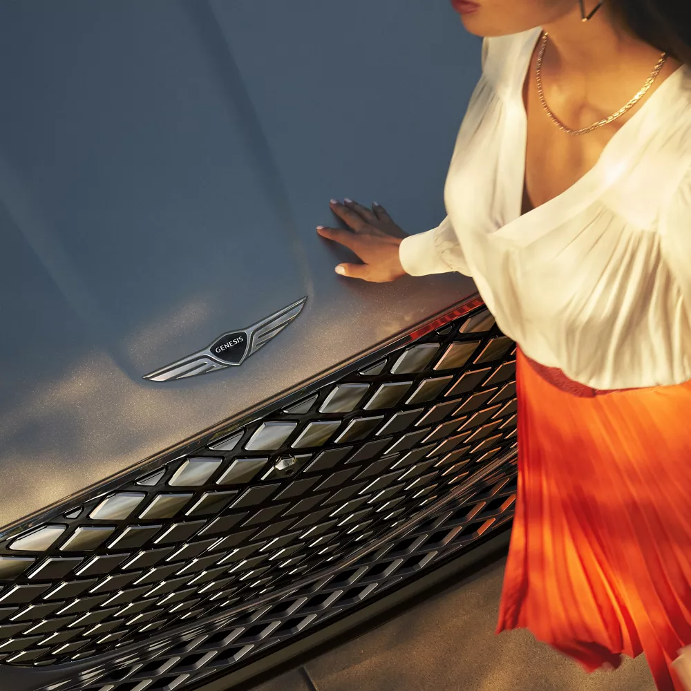 Closeup of woman in orange skirt & white shirt leaning on hood of Genesis Electrified GV70