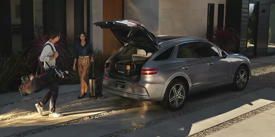 Genesis Electrified GV70 parked in driveway of modern home with family loading luggage