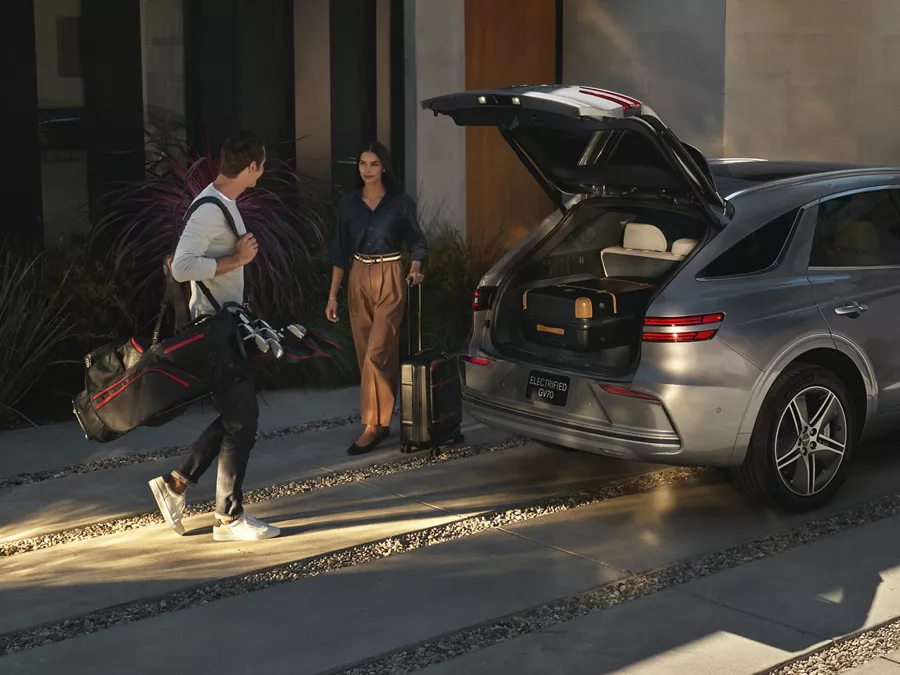 Genesis Electrified GV70 parked in driveway of modern home with family loading luggage