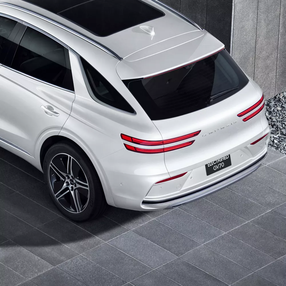 3/4 rear aerial close-up of white Genesis Electrified GV70 parked under minimalist concrete building