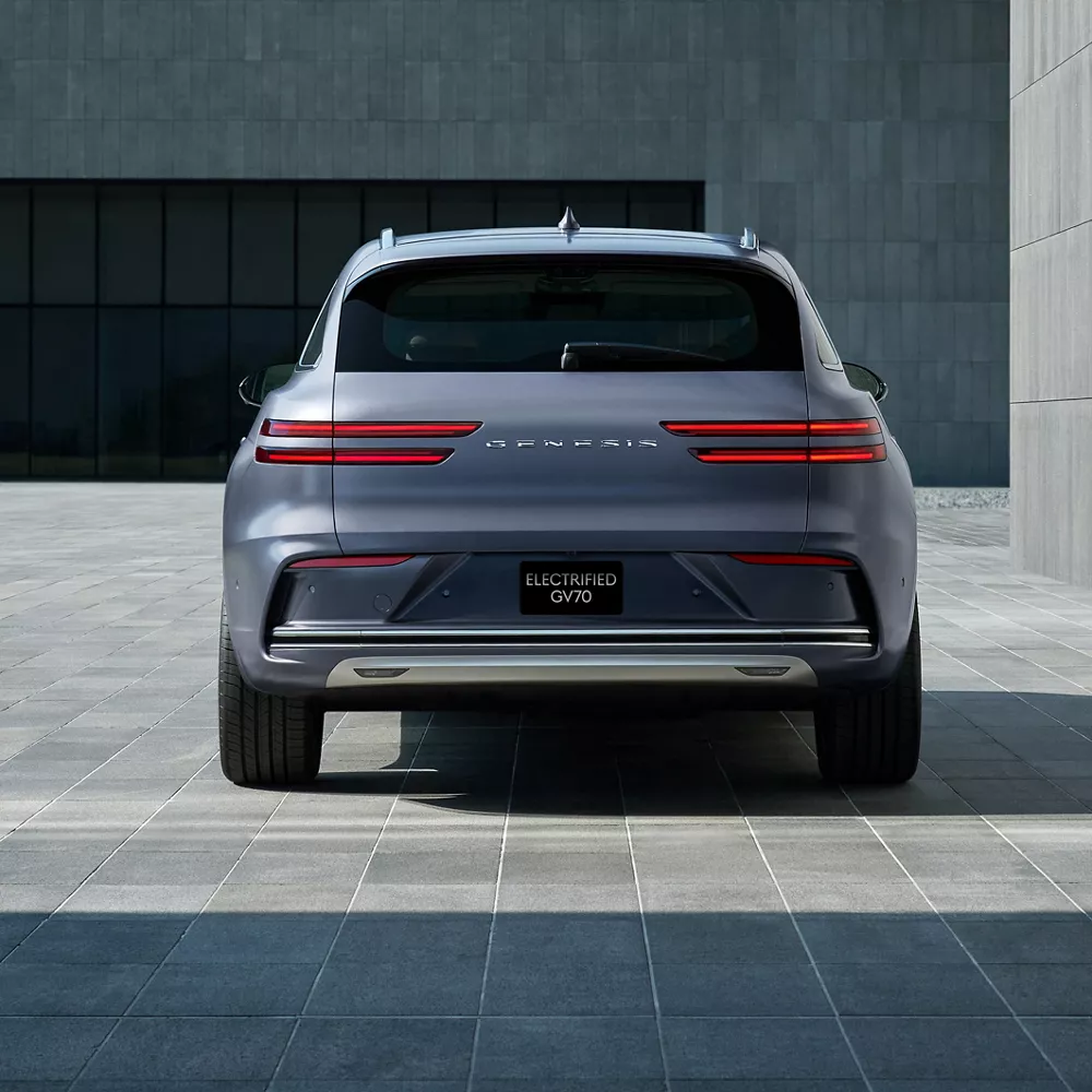 Rear view of Genesis Electrified GV70 in Ceres Blue parked in modern stone courtyard