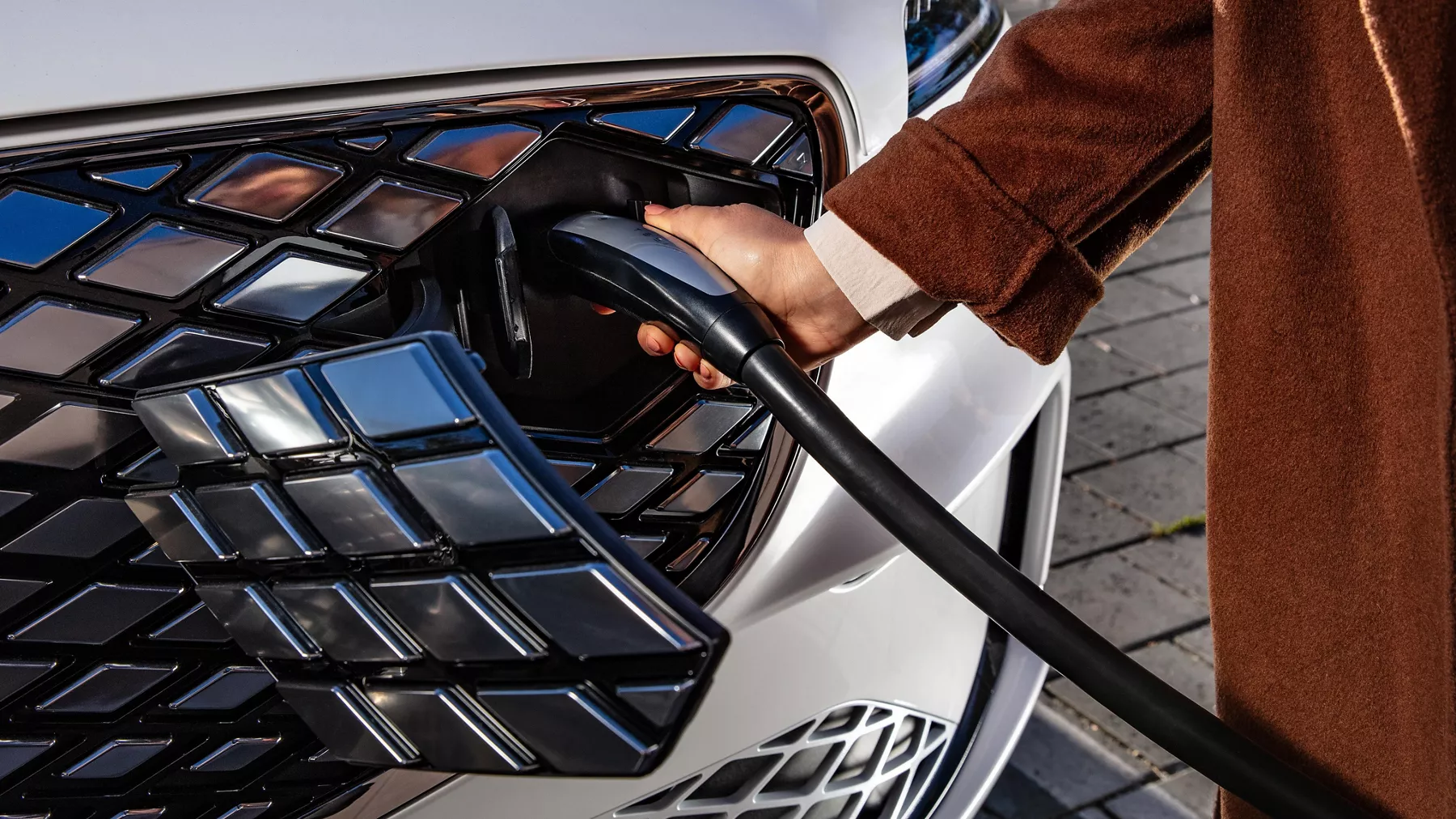 Close-up of hand holding charger to front port behind grille of white Genesis Electrified GV70