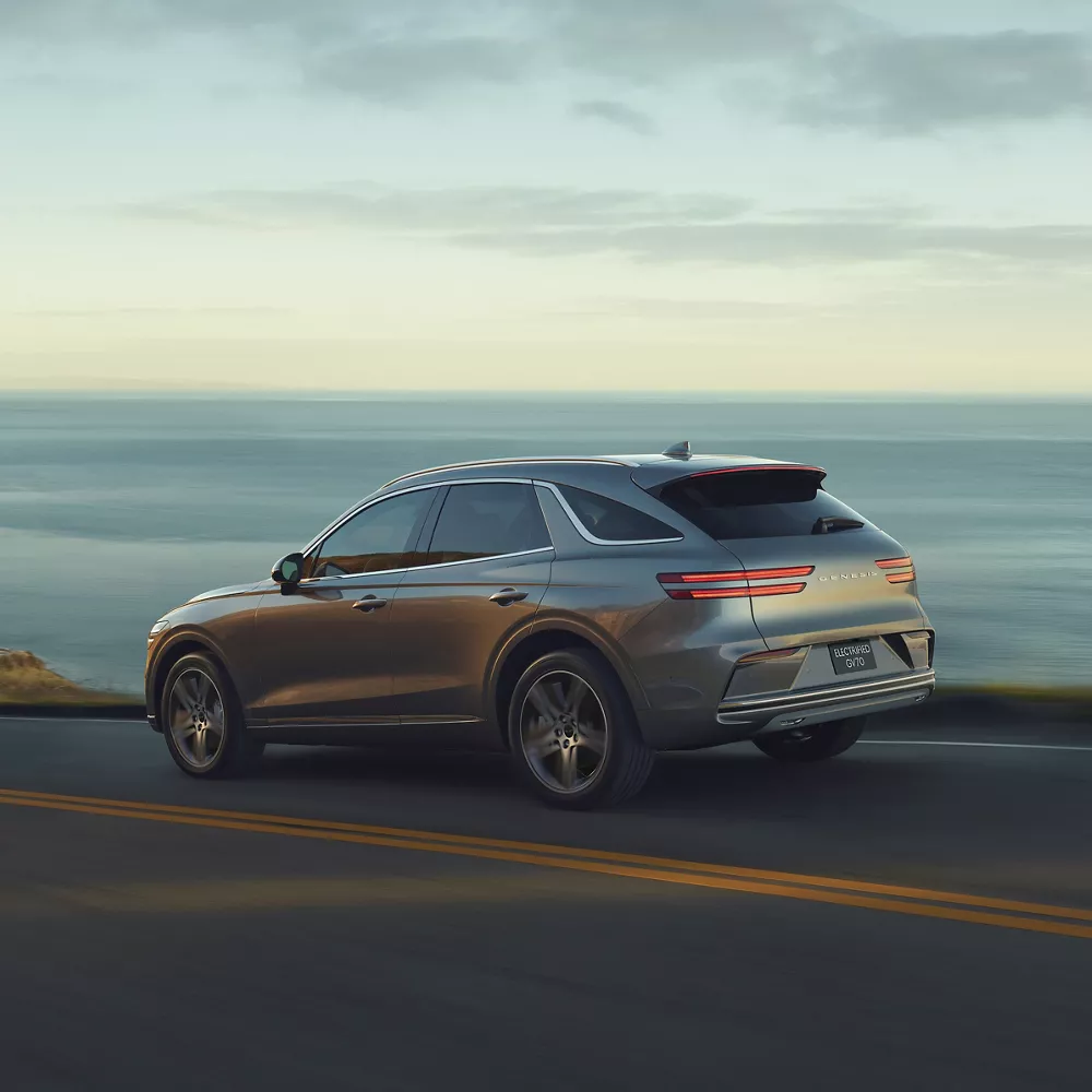 7/8 Rear Driver Side Genesis Electrified GV70 Prestige in Savile Silver in motion on coastal highway