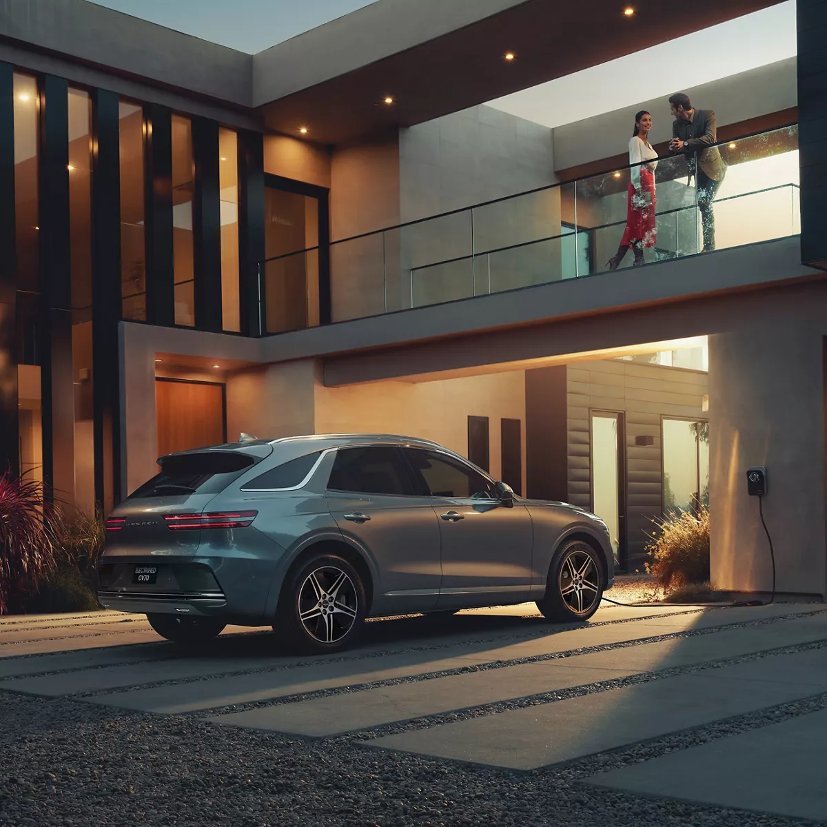 3/4 rear passenger side view of Genesis Electrified GV70 parked outside modern home at night