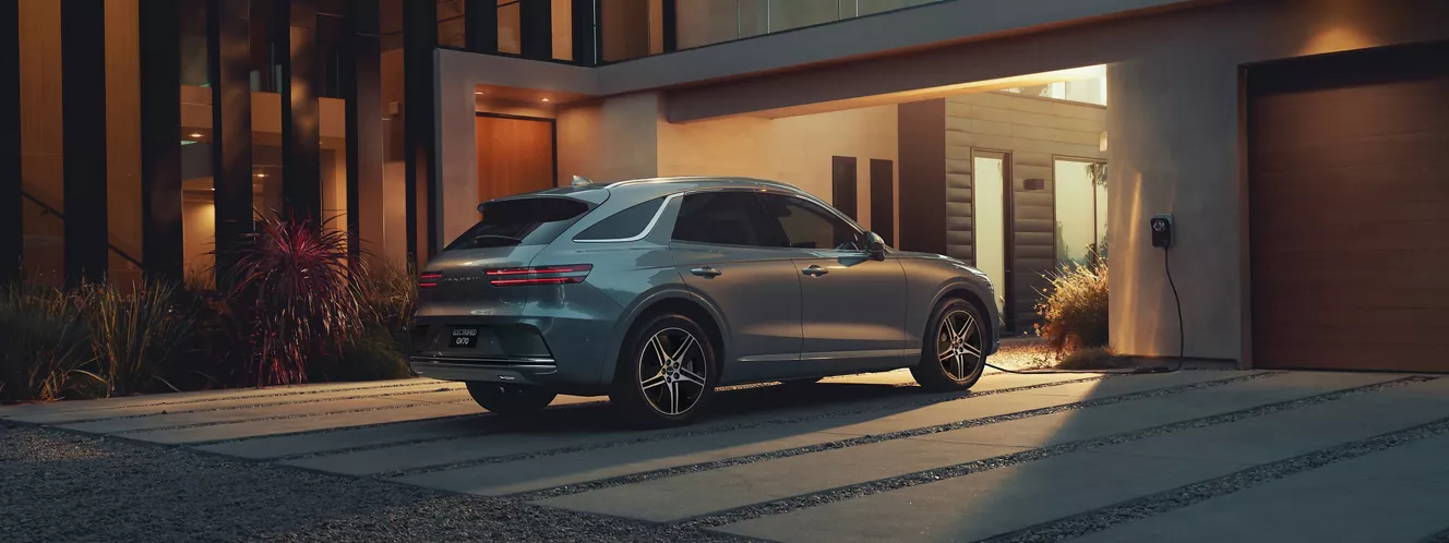 3/4 rear passenger side view of Genesis Electrified GV70 parked outside modern home at night