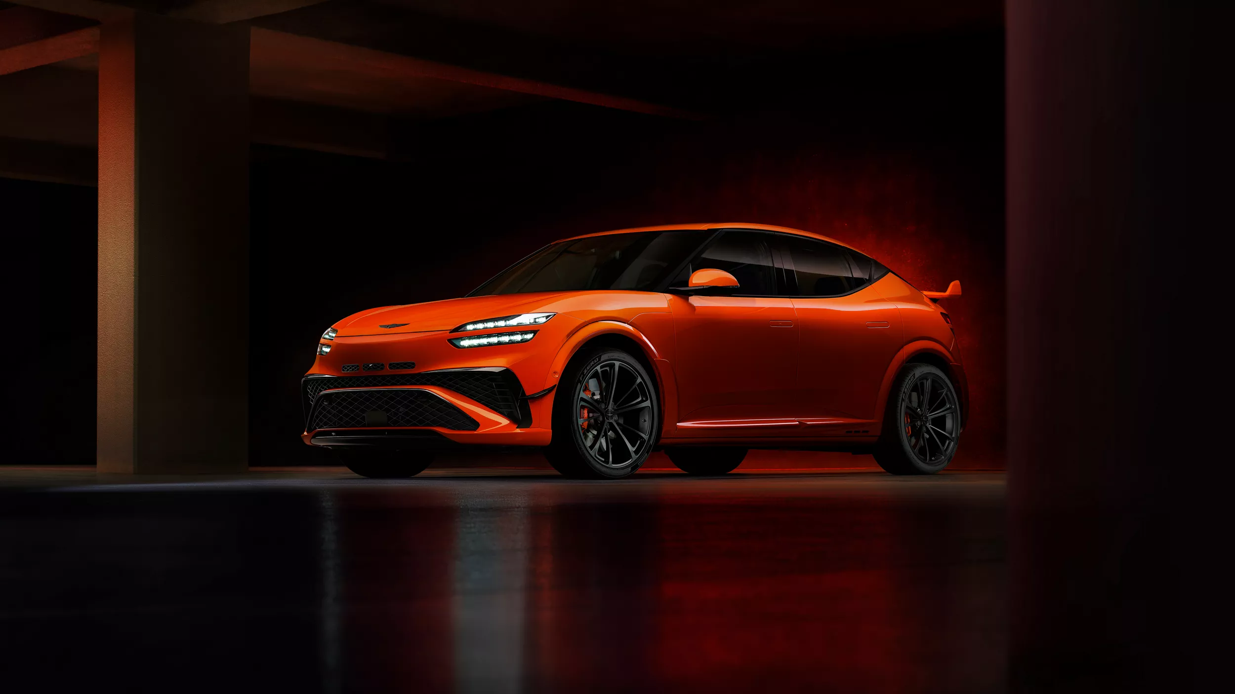 3/4 driver side view of 2027 Genesis GV60 Magma in orange, parked in dimly lit building