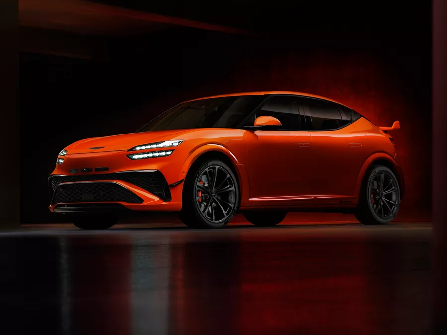 3/4 front driver side view of 2027 Genesis GV60 Magma in orange, parked in dimly lit garage