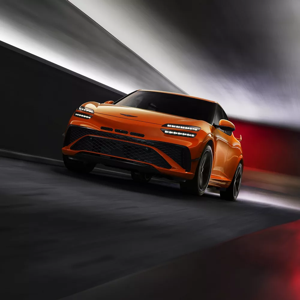 3/4 front driver side view of 2027 Genesis GV60 Magma in orange driving through tunnel