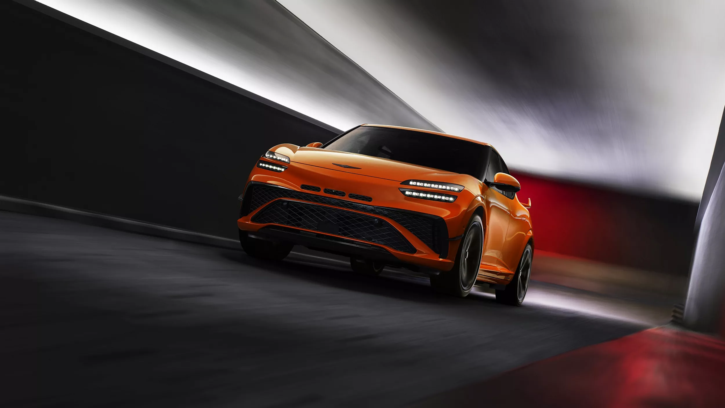 Ground level 3/4 driver side view of 2027 Genesis GV60 Magma in orange, in motion