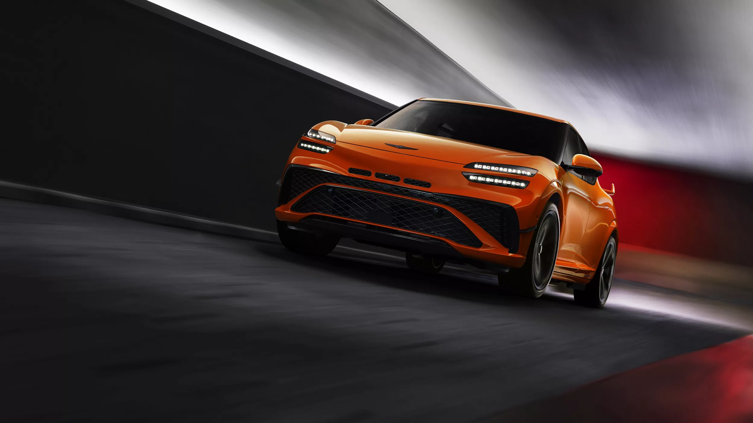 Ground level 3/4 driver side view of 2027 Genesis GV60 Magma in orange, in motion