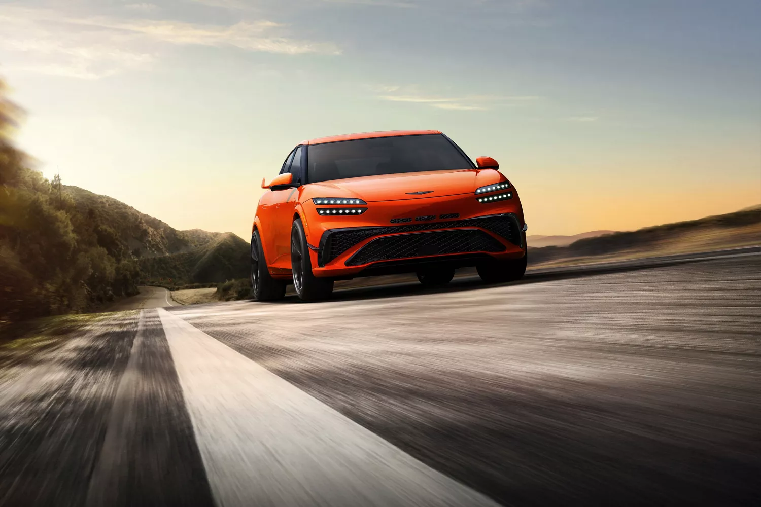 Low 3/4 front passenger side view of 2027 Genesis GV60 Magma in orange driving mountain road