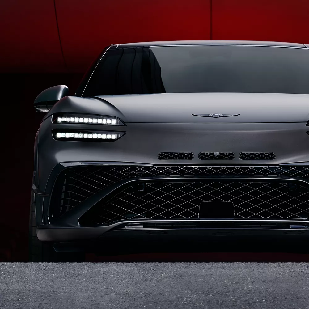 Close up front angle of Genesis 2027 GV60 Magma driving up from a parking ramp