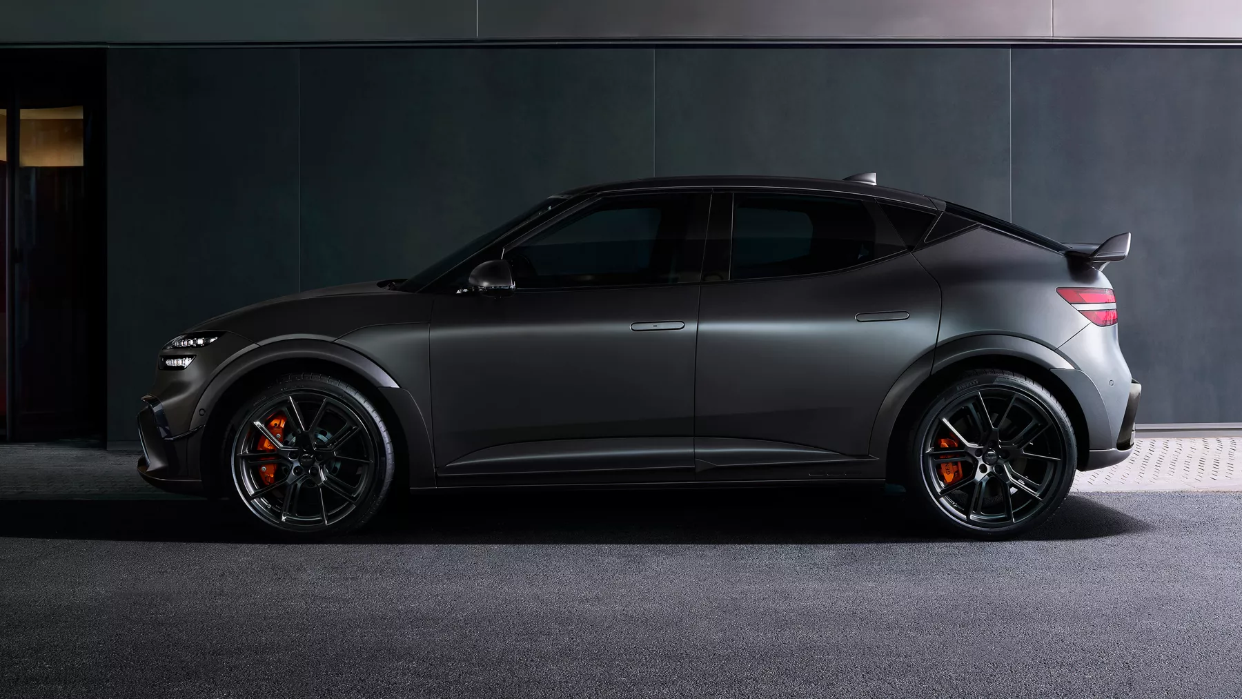 Driver side profile of 2027 Genesis GV60 Magma in Makalu Grey Matte parked in dimly lit garage